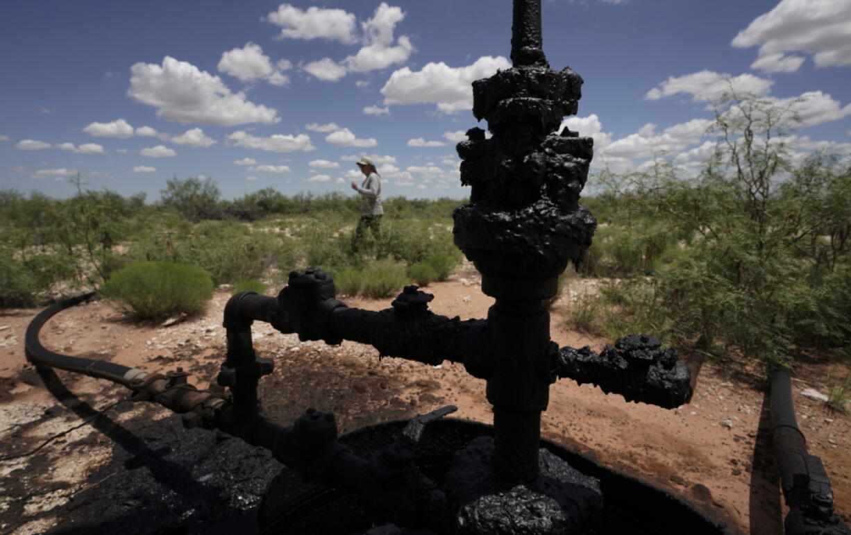 Ashley Williams Watt walks near a wellhead and flowline at her ranch, Friday, July 9, 2021, near Crane, Texas. The wells on Watt's property seem to be unplugging themselves. Some are leaking dangerous chemicals into the ground, which are seeping into her cattle's drinking water. And she doesn't know how long it's been going on.