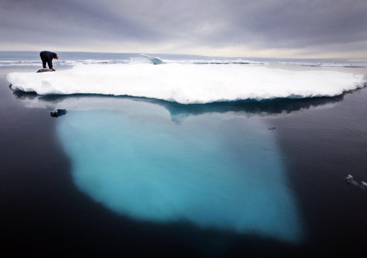 FILE - In this file photo dated July 2007,  an Inuit seal hunter touches a dead seal atop a melting iceberg near Ammassalik Island, Greenland.