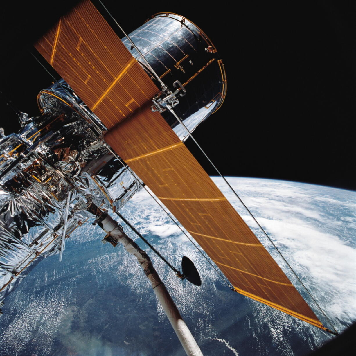 FILE - In this April 25, 1990 photograph provided by NASA, most of the giant Hubble Space Telescope can be seen as it is suspended in space by Discovery's Remote Manipulator System (RMS) following the deployment of part of its solar panels and antennae.   The Hubble Space Telescope should be back in action soon, Friday, July 16, 2021, following a tricky, remote repair job by NASA. The orbiting observatory went dark in mid-June, with all astronomical viewing halted.