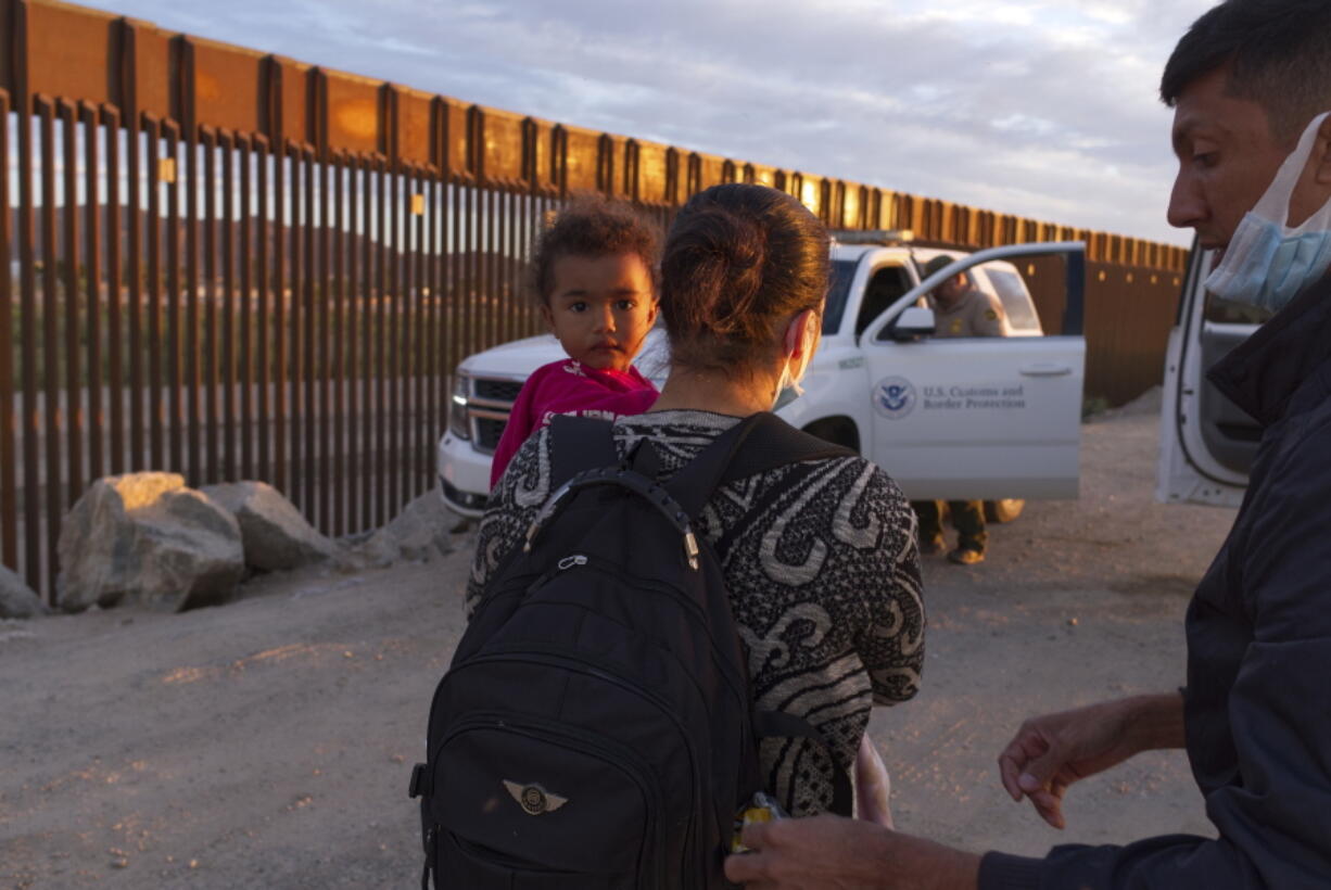 FILE - In this June 10, 2021, file photo, a migrant family from Brazil waits to be processed by U.S. Border Patrol agents after passing through a gap in the border wall from Mexico in Yuma, Ariz. U.S. officials say attempted border crossings by migrants traveling in family groups that include children increased in June by a quarter over the previous month amid rising summer temperatures in the inhospitable deserts and mountain terrain of the American Southwest.