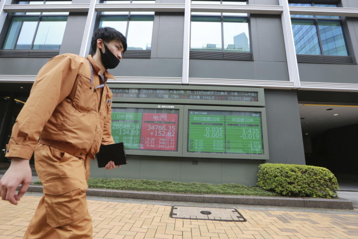 A man walks by an electronic stock board of a securities firm in Tokyo, Monday, July 5, 2021. Shares were mixed Monday in Asia in quiet trading, with U.S. markets set to be closed for the Independence Day holiday.