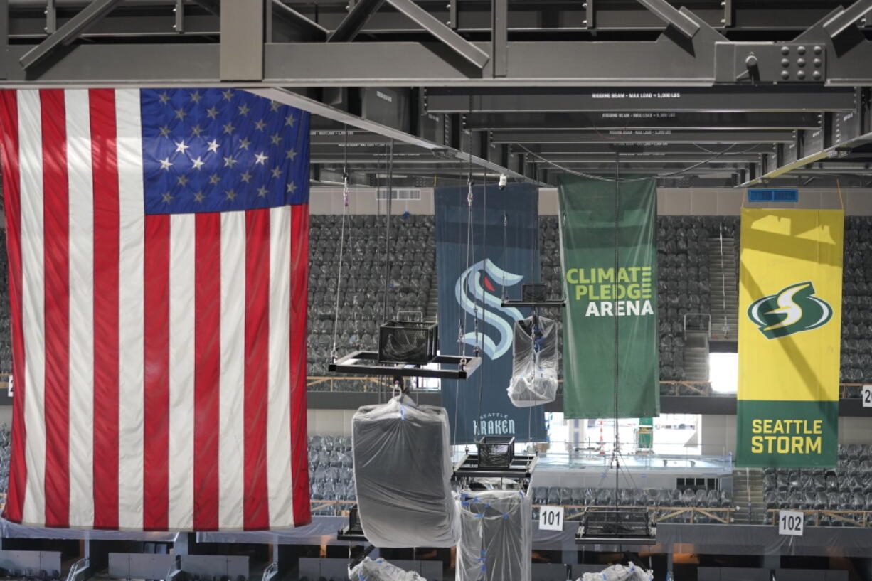 United States and team flags hang in the rafters of the Climate Pledge Arena during a media tour of the facility, Monday, July 12, 2021, in Seattle. The arena will be the home of the NHL hockey team Seattle Kraken and the WNBA Seattle Storm basketball team as well as hosting concerts and other performing arts events. (AP Photo/Ted S.