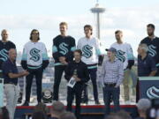 New Seattle Kraken NHL hockey players, back row from left, Mark Giordano, Brandon Tanev, Jamie Oleksiak, Hadyn Fluery, Jordan Eberle and Chris Dreidger stand on stage with Kraken owners David Wright, front left, Jerry Bruckheimer, front center, and Andy Jassy, front second from right, and Kraken general manager Ron Francis, front right, Wednesday, July 21, 2021, after being introduced during the Kraken's expansion draft event in Seattle. Jassy is also president and CEO of Amazon.com. (AP Photo/Ted S.