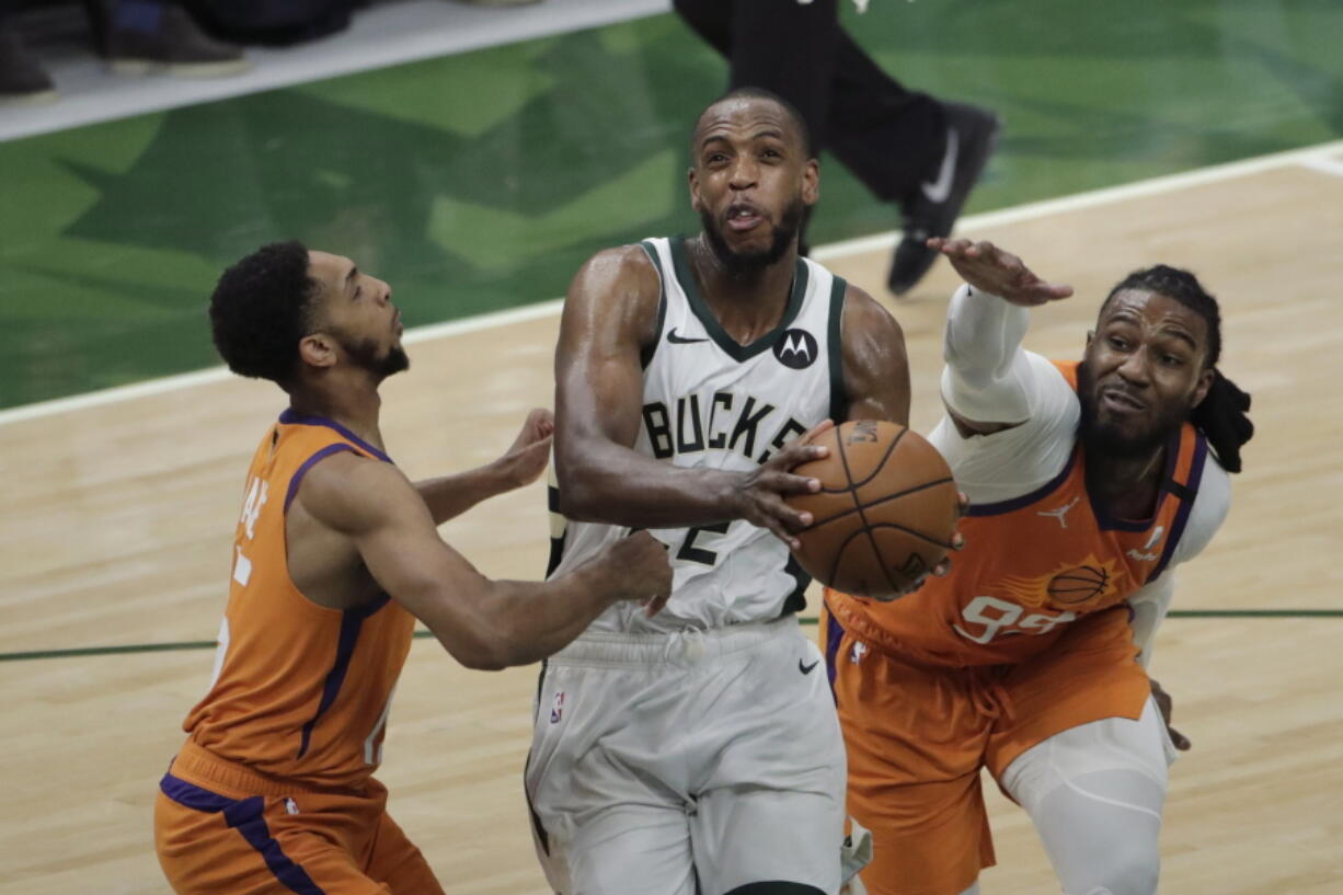 Milwaukee Bucks forward Khris Middleton, center, drives to the basket between Phoenix Suns guard Cameron Payne, left, and forward Jae Crowder, right, during the second half of Game 4 of basketball's NBA Finals Wednesday, July 14, 2021, in Milwaukee.