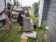 Carl Rocha, left, and Patrick Plummer, with Bills Heating & A/C Install air conditioning and a new furnace at a home on East Wabash Street, Wednesday, June 23, 2021, in Spokane, Wash. With temperatures forecast to hit over 100 degrees by Sunday, a rush of customers are keeping local A/C installers busy.