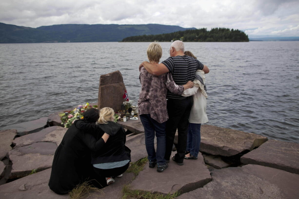 FILE - In this Monday, July 25, 2011 file photo, relatives of a victim gather to observe a minute's silence on a campsite jetty on the Norwegian mainland, across the water from Utoya island, seen in the background, where people have been placing floral tributes in memory of those killed in the shooting massacre on the island.  At 3.25 p.m. on July 22, 2021, a ray of sun should have illuminated the first of 77 bronze columns on a lick of land opposite Utoya island outside Oslo. Over the next 3 hours and 8 minutes, it would have brushed each column in turn, commemorating every person killed by right-wing terrorist Anders Breivik. But on the ten-year anniversary of the terror, the memorial remains a construction site.