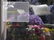 A sign noting the death of Barnett Moss is displayed as memorial flowers are reflected in the window during a memorial service for Moss -- who died last week during the Pacific Northwest Heatwave -- on the front porch entryway of the United Churches of Olympia, Friday, July 9, 2021, in Olympia, Wash. Moss slept nightly on the cement in front of the church and during the day could usually be found reading books on a bench inside the Capitol Rotunda in front of the Washington Legislature House chambers. (AP Photo/Ted S.