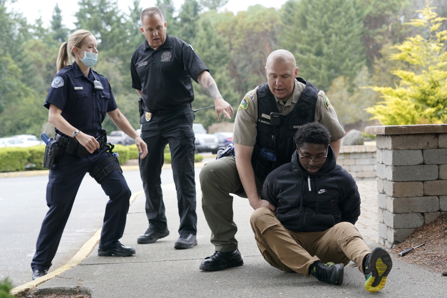 Kevin Burton-Crow, upper-right, of the Thurston Co. Sheriff's Dept., handcuffs Naseem Coaxum, right, an actor playing the role of a person causing a disturbance at a convenience store, during a training class at the Washington state Criminal Justice Training Commission, Wednesday, July 14, 2021, in Burien, Wash., instructor Ken Westphal, second from left, an officer with the Lacey Police Dept., and LeAnne Cone, left, of the Vancouver Police Dept., look on. Washington state is embarking on a massive experiment in police reform and accountability following the racial justice protests that erupted after George Floyd's murder last year, with nearly a dozen new laws that took effect Sunday, July 25 but law enforcement officials remain uncertain about what they require in how officers might respond -- or not respond -- to certain situations, including active crime scenes and mental health crises. (AP Photo/Ted S.