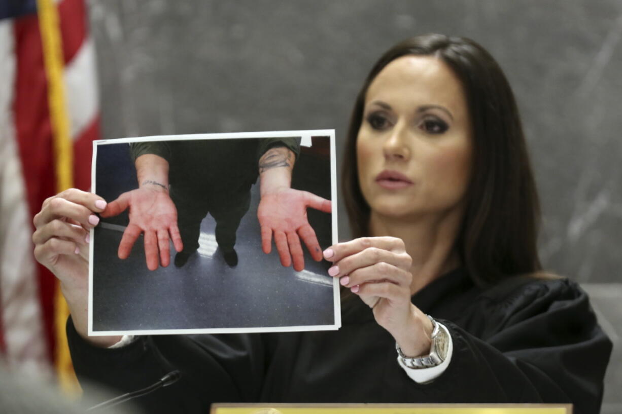 Judge Elizabeth Scherer holds a photograph of the hands of Broward jail guard Sgt. Ray Beltran after a November 2018 altercation between Beltran and Parkland school shooter Nikolas Cruz during Cruz's pre-trial hearing at the Broward County Courthouse in Fort Lauderdale, Fla., Wednesday, July 14, 2021, on four criminal counts stemming from his alleged attack on a Broward jail guard in November 2018. Cruz is accused of punching Sgt. Ray Beltran, wrestling him to the ground and taking his stun gun.