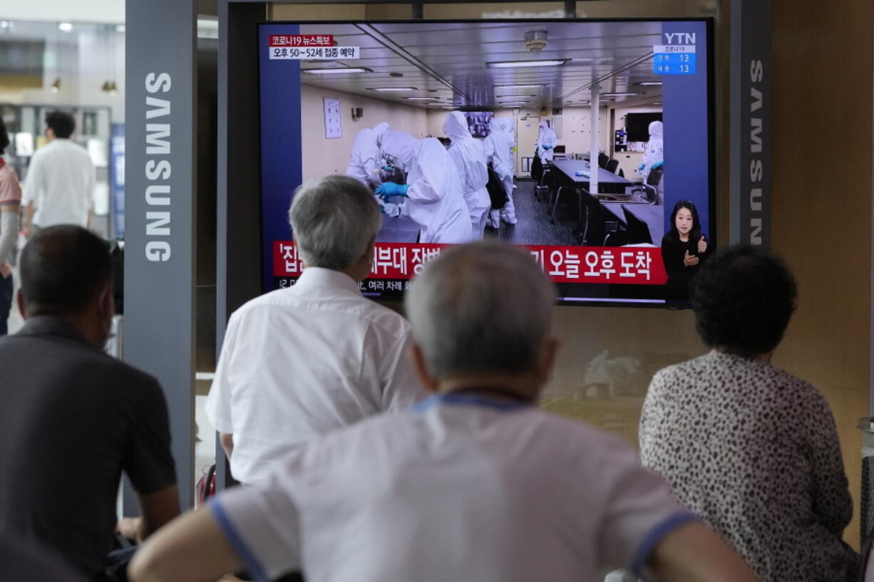 People watch a TV showing an image of South Korean service members wearing protective clothes disinfect inside the naval destroyer Munmu the Great during a news program at the Seoul Railway Station in Seoul, South Korea, Tuesday, July 20, 2021. South Korea's prime minister on Tuesday apologized for "failing to carefully take care of the health" of hundreds of sailors who contracted the coronavirus on a navy ship taking part in an anti-piracy mission off East Africa.