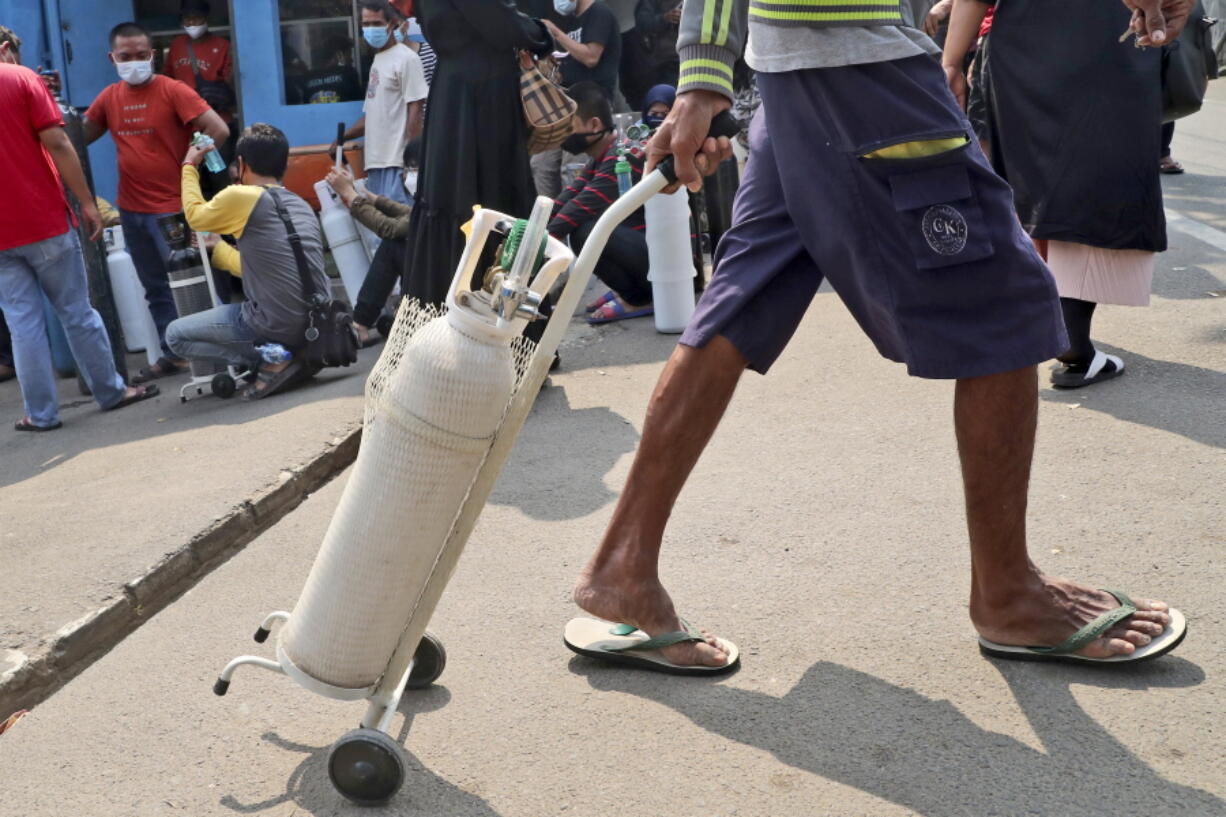 A man leaves with his full oxygen canister as others wait to refill their tanks at a recharging station in Jakarta, Indonesia, Friday, July 9, 2021. Just two months ago, Indonesia was coming to a gasping India's aid with thousands tanks of oxygen. Now, the Southeast Asia country is running out of oxygen as it endures a devastating wave of coronavirus cases and the government is seeking emergency supplies from other countries, including Singapore and China.