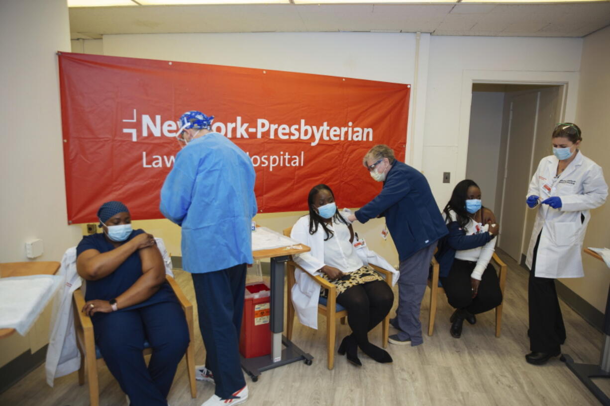 FILE - In this Friday, Jan. 8, 2021, file photo doctors inject sisters Claudia Scott-Mighty, left, Althea Scott-Bonaparte, who are patient care directors, and Christine Scott, an ICU nurse, with their second shot of the Pfizer vaccine at NewYork-Presbyterian Lawrence Hospital, in Bronxville, N.Y. The private New York-Presbyterian hospital system announced in June that it will require its 48,000 employees to be vaccinated unless they have a valid exemption. Workers in New York City-run hospitals and health clinics will have to get vaccinated or get tested weekly under a policy announced Wednesday, July 21, to battle a rise in COVID-19 cases fueled by the highly contagious delta variant.