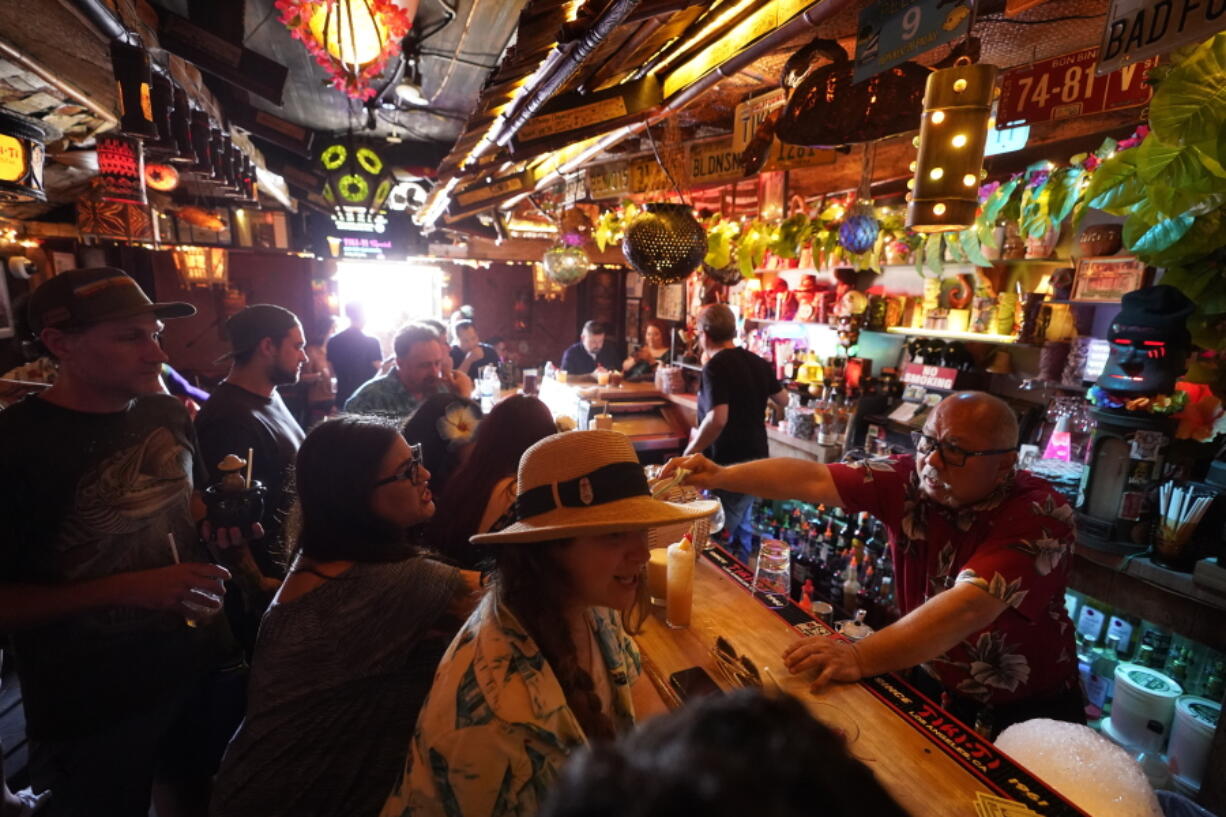 FILE - In this Wednesday, July 7, 2021, file photo, patrons enjoy cold tropical cocktails in the tiny interior of the Tiki-Ti bar as it reopens on Sunset Boulevard in Los Angeles. COVID-19 cases have doubled over the past three weeks, driven by the fast-spreading delta variant, lagging vaccination rates in some states and Fourth of July gatherings.  Los Angeles County public health officials have urged people to resume wearing masks indoors regardless of their vaccination status.