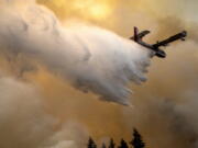 A scoop plane drops water onto a burning ridge where a fire line had been created by crews of wildland firefighters, Monday, July 12, 2021, at the Lick Creek Fire, south of Asotin, Wash.