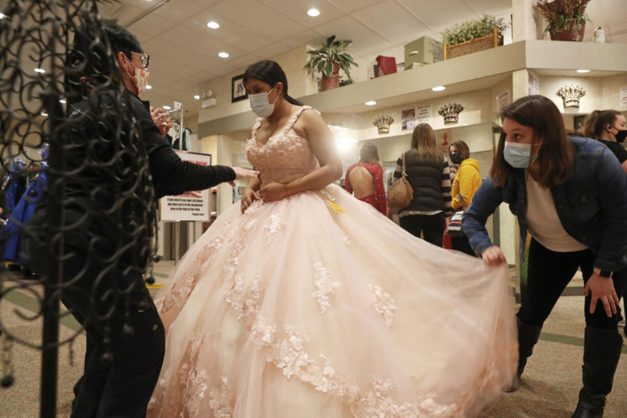 Nataly Contreras, 14, tries on a quinceanera dress as her sister-in-law, Cristal Contreras, right, and Peaches Boutique owner Barb Surdej, left, help at the boutique, 5915 S. Archer Ave., Saturday, Feb. 27, 2021, in Chicago. (John J.