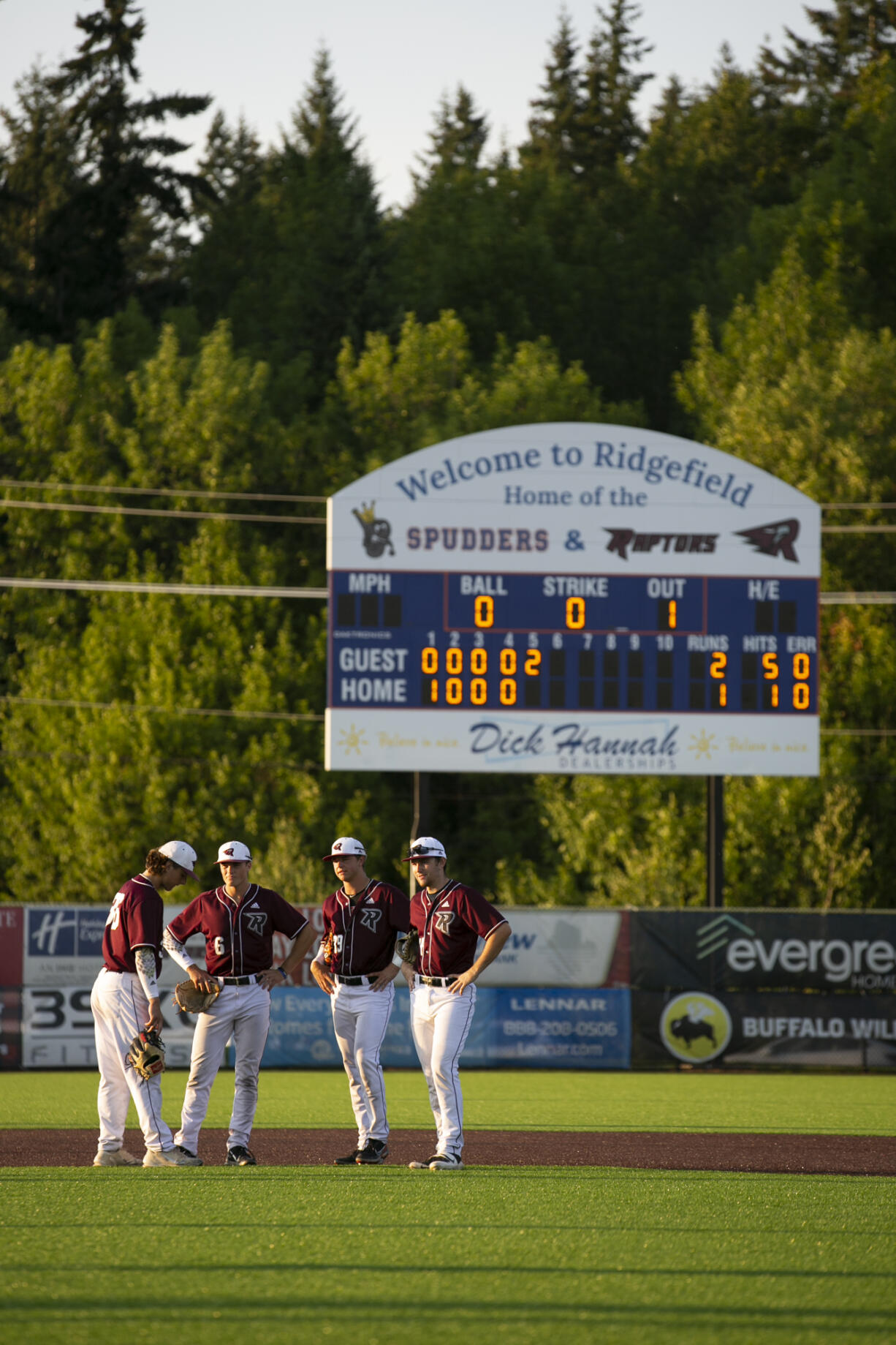 Ridgefield Raptors players gather in the infield as pitcher Carson Walters warms up at the mound in the fith inning against the Cowlitz Black Bears at Ridgefield Outdoor Recreation Complex on Wednesday, August 4, 2021.