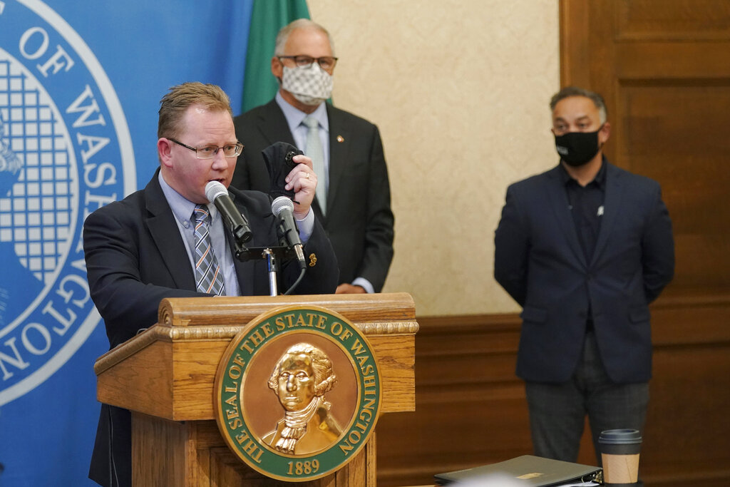 Washington State Superintendent of Public Instruction Chris Reykdal, left, holds up a face mask as he speaks at a news conference, along with Gov. Jay Inslee, center, and Secretary of Health Umair A. Shah, right, at the Capitol, Wednesday, Aug. 18, 2021, in Olympia, Wash. Inslee announced that Washington state is expanding its vaccine mandate to include all public, charter and private school teachers and staff, as well as those working at the state's colleges and universities. The Governor also expanded the statewide indoor mask mandate in place for non-vaccinated individuals to include those who are vaccinated. (AP Photo/Ted S.