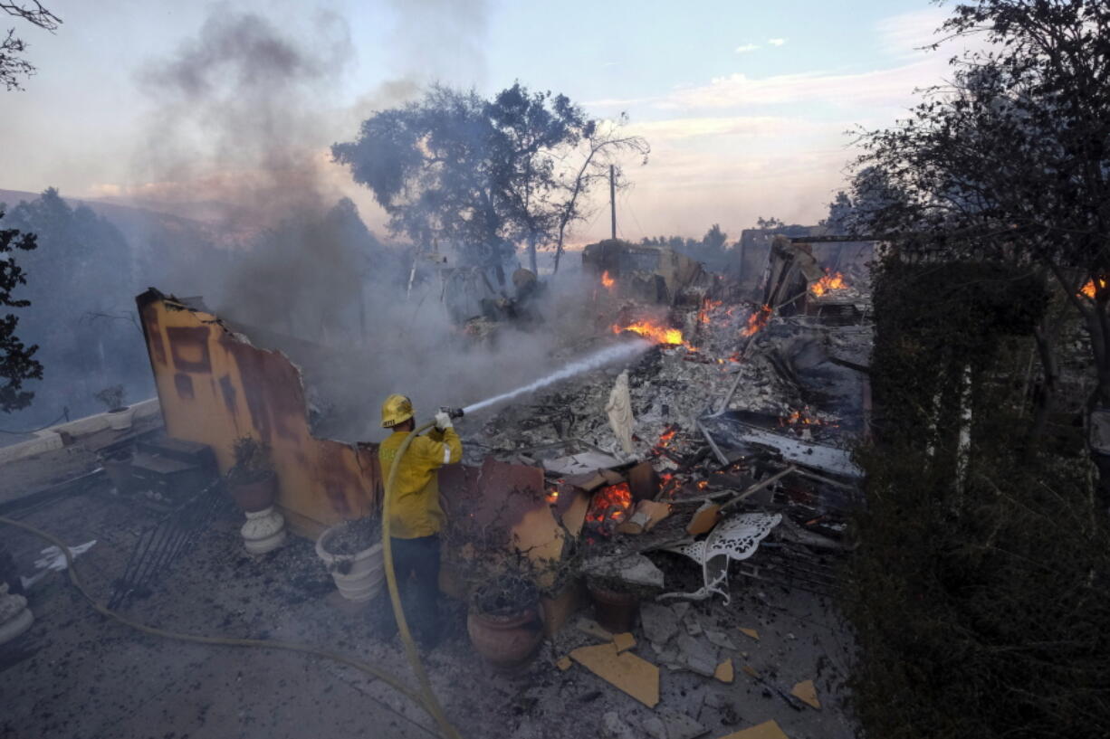 A firefighter tries to extinguish the flames at a burning house as the South Fire burns in Lytle Creek, San Bernardino County, north of Rialto, Calif., Wednesday, Aug. 25, 2021. (AP Photo/Ringo H.W.