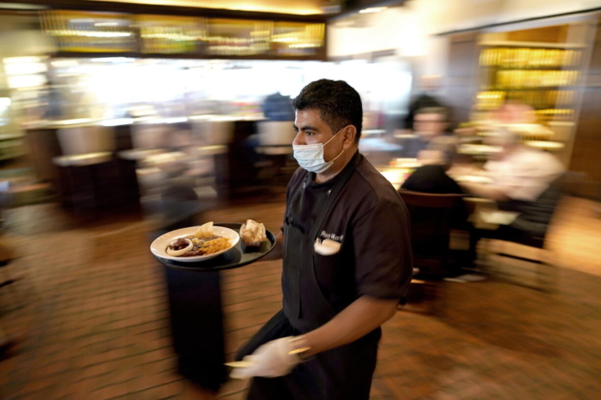 FILE - In this March 10, 2021, file photo Marcelino Flores wears a face mask as he delivers food to a table at Picos restaurant in Houston. Half of American workers are in favor of vaccine requirements at their workplaces, according to a new poll, as such mandates gain traction following the U.S. government's full approval to Pfizer's COVID-19 vaccine. That's according to a poll from The Associated Press-NORC Center for Public Affairs Research. (AP Photo/David J.