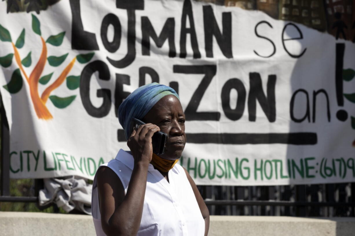 A woman speaks on the phone in front of a sign in Haitian Creole during a news conference held by a coalition of housing justice groups to protest evictions, Friday, July 30, 2021, outside the Statehouse in Boston.