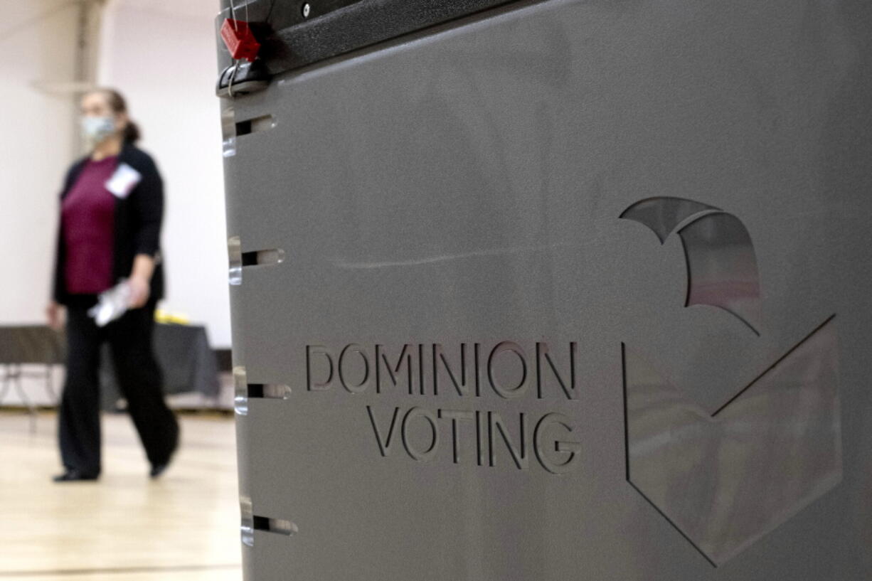 FILE - In this Jan. 4, 2021, file photo a worker passes a Dominion Voting ballot scanner while setting up a polling location at an elementary school in Gwinnett County, Ga., outside of Atlanta. A federal magistrate on Wednesday, Aug. 4, levied penalties against two Colorado attorneys for filing a class-action lawsuit that alleged the 2020 presidential election was stolen from Donald Trump. The now-dismissed lawsuit relied on baseless conspiracy theories spread by Trump and his supporters and named elected officials in four swing states, Facebook, the company's found Mark Zuckerberg and Denver-based Dominion Voting Systems, whose election machines were at the center of some of the most fevered speculation.