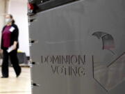 FILE - In this Jan. 4, 2021, file photo a worker passes a Dominion Voting ballot scanner while setting up a polling location at an elementary school in Gwinnett County, Ga., outside of Atlanta. Republican efforts to question the results of the 2020 election have led to two significant breaches of voting software that have alarmed election security experts who say they have increased the risk to elections in jurisdictions that use the equipment.