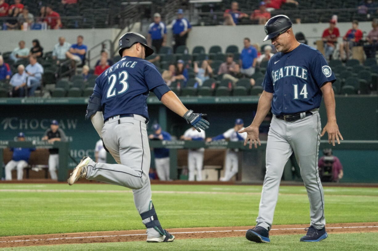 Seattle Mariners' Ty France (23) is congratulated by third base coach Manny Acta (14) after hitting a two-run home run off Texas Rangers relief pitcher Joe Barlow during the 11th inning of a baseball game Thursday, Aug. 19, 2021, in Arlington, Texas. Seattle won 9-8.