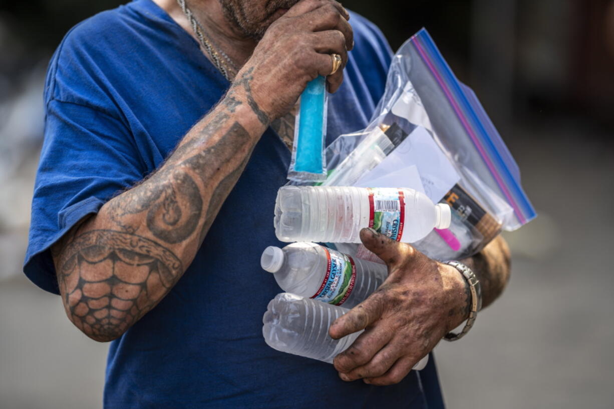 Chad Messenger collects cooling supplies including bottled water donated by the Cascadia Behavioral Healthcare's street outreach team on Thursday, Aug. 12, 2021, in Portland, Ore.