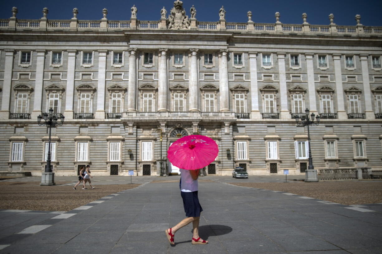 A woman with an umbrella walks past the Royal Palace during a heatwave in Madrid, Spain, Friday, Aug. 13, 2021. Stifling heat is gripping much of Spain and Southern Europe, and forecasters say worse is expected to come.