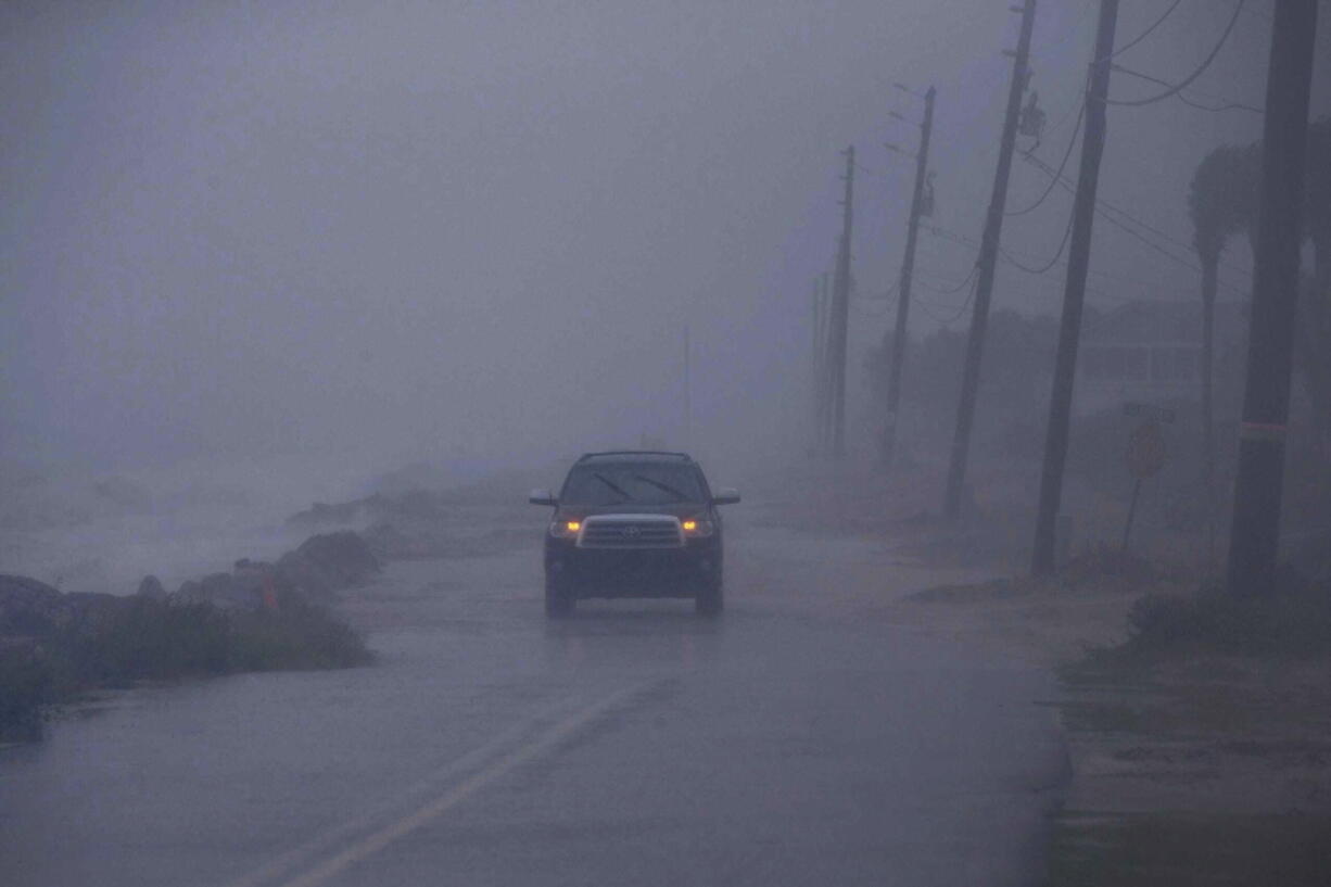 In a downpour, an SUV driver makes their way down Alligator Drive in Alligator Point, Fla., as waves crash onto the road during Tropical Storm Fred, Monday, Aug. 16, 2021.