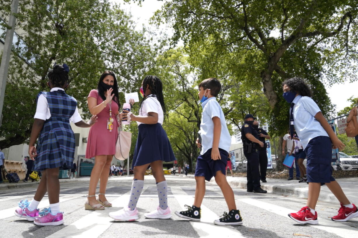 Teacher Vanessa Rosario greets students outside of iPrep Academy on the first day of school, Monday, Aug. 23, 2021, in Miami. Schools in Miami-Dade County opened Monday with a strict mask mandate to guard against coronavirus infections.