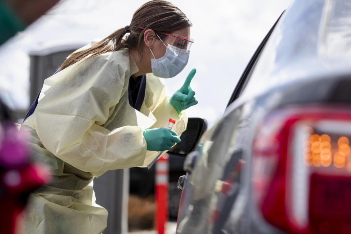 FILE - In this March 17, 2020 file photo, Ashley Layton, an LPN at St. Luke's Meridian Medical Center, communicates with a person before taking swab sample at a special outdoor drive-thru screening station for COVID-19 in Meridian, Idaho.