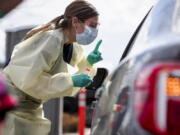 FILE - In this March 17, 2020 file photo, Ashley Layton, an LPN at St. Luke's Meridian Medical Center, communicates with a person before taking swab sample at a special outdoor drive-thru screening station for COVID-19 in Meridian, Idaho.