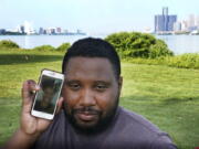 With the cities of Windsor, Canada, left, and Detroit, right, in the background, Quintin Sweat Jr. poses with his fiancee Renee Harrison, seen on his phone, Tuesday on Belle Isle in Detroit.