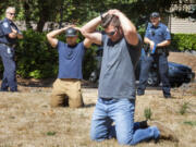 Recruit officer Seth Anderson, right, with the Vancouver Police Department apprehends "suspects" Chad Sommerfield, foreground, a recruit with the Everett Police Department and Junior Alvidrez, second from left, a recruit with the King County Sheriff's department after a mock fight during an academy class at the Washington Criminal Justice Training Center in Burien, Washington on Wednesday, August 18, 2021 where recruits are learning and using less-than-lethal force alternatives.  At left is Steve Woodward, a TAC officer with the Washington State Criminal Justice Training Commission, who is watching the operation and then giving advice and instructions regarding improvements that can be made regarding how the arresting recruit officers handled the situation. (Ellen M.