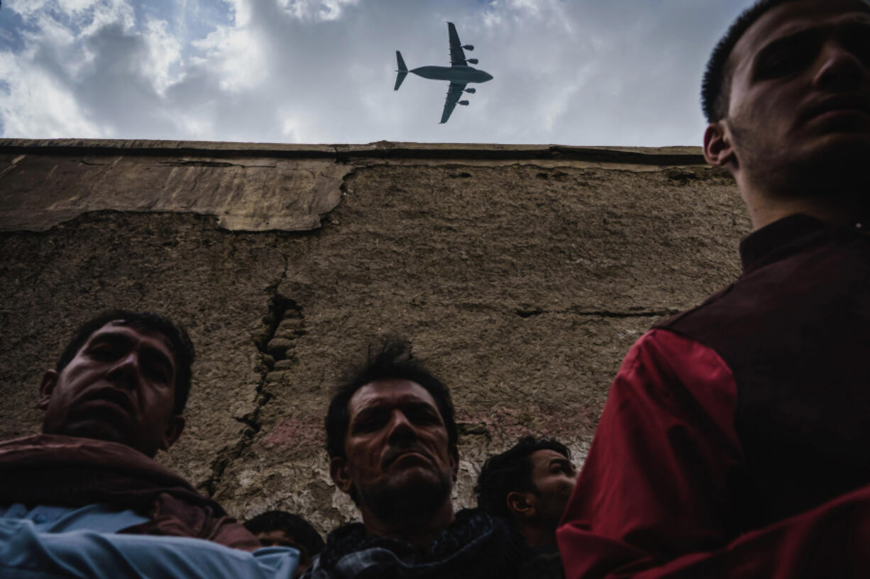 A military transport plane flies over as Afghans mourn family members who died Sunday, Aug. 29, 2021, in Kabul, Afghanistan.