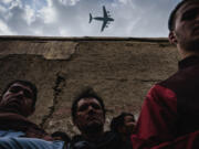 A military transport plane flies over as Afghans mourn family members who died Sunday, Aug. 29, 2021, in Kabul, Afghanistan.