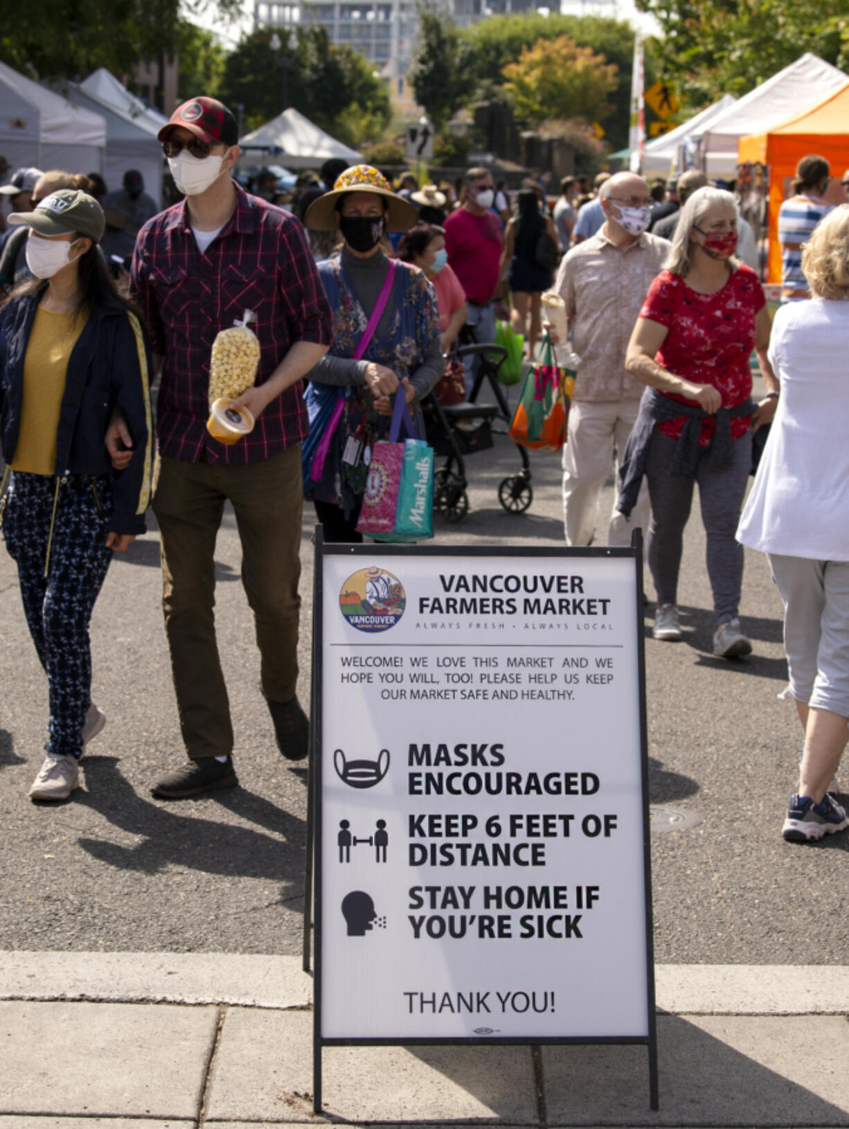 Guests walk past a sandwich board that alerts people to the COVID-19 guidelines recommended by the Vancouver Farmers Market on Saturday in downtown Vancouver.