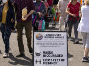 Guests walk past a sandwich board that alerts people to the COVID-19 guidelines recommended by the Vancouver Farmers Market on Saturday in downtown Vancouver.