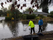 Lucy, left, and Steve Hawkins of Vancouver lend a hand Monday afternoon as a clogged rain gutter leads to a flooded intersection along McGillivray Boulevard.