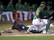 Seattle Mariners' Jake Bauers slides home safe on a throwing error by Paul Blackburn as Oakland Athletics' Yan Gomes applies the tag during the second inning of a baseball game in Oakland, Calif., Tuesday, Sept. 21, 2021.