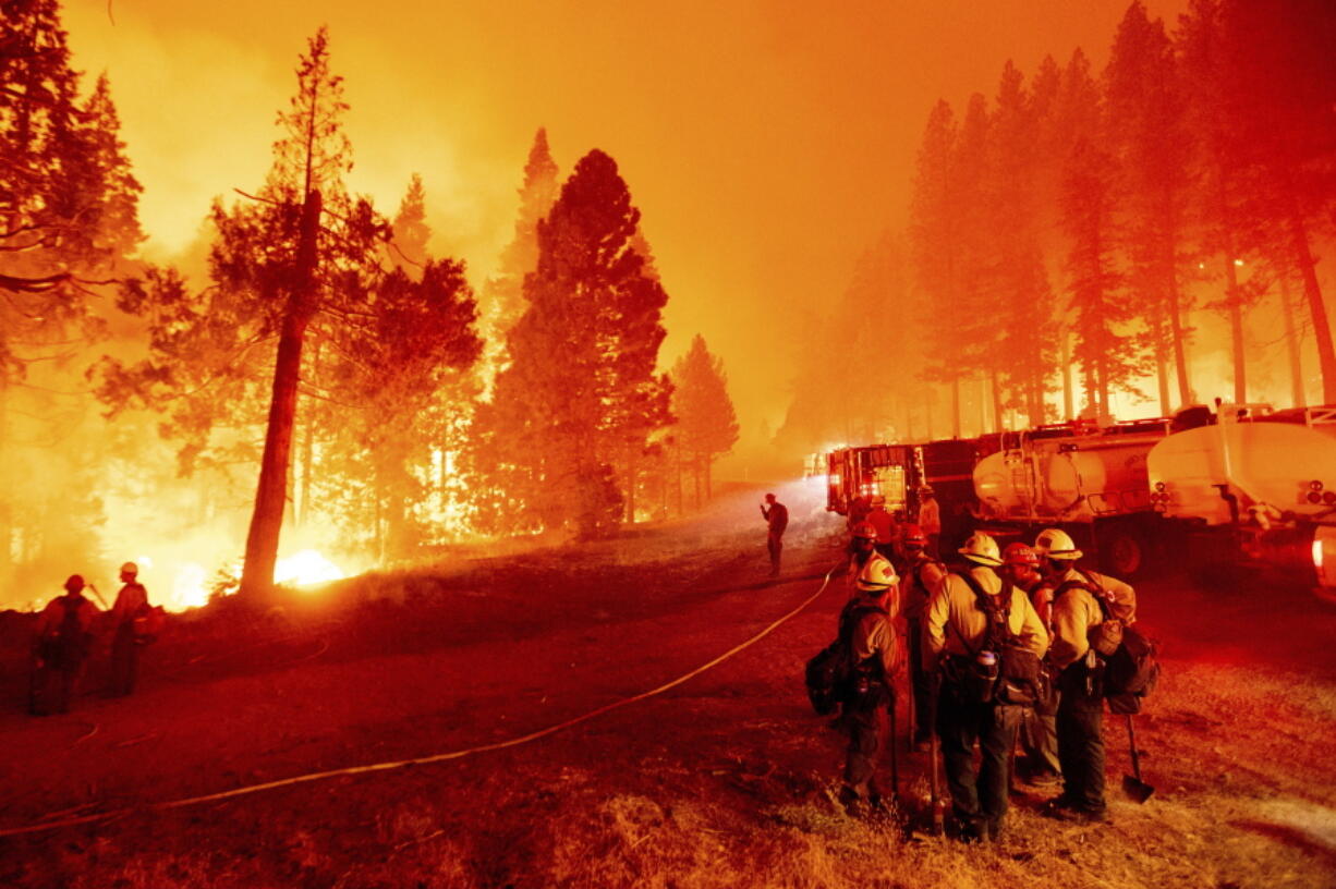 FILE - In this Thursday, Aug. 26, 2021 file photo, the Caldor Fire burns along both sides of Highway 50 as firefighters work to stop its eastward spread in Eldorado National Forest, Calif.. Last week, managers overseeing the fight against the massive wildfire scorching California's Lake Tahoe region thought they could have it contained by the start of this week. Instead, on Monday, Aug. 30, 2021, the Caldor Fire crested the Sierra Nevada, forcing the unprecedented evacuation of all 22,000 residents of South Lake Tahoe.