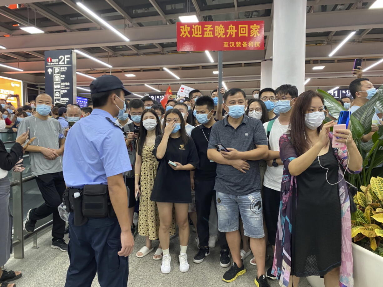 Police stand guard as supporters of Huawei CFO Meng Wanzhou gather at Shenzhen Bao'an International Airport in Shenzhen in southern China's Guangdong Province, Saturday, Sept. 25, 2021. China's government was eagerly anticipating the return of a top executive from global communications giant Huawei Technologies on Saturday following what amounted to a high-stakes prisoner swap with Canada and the U.S.