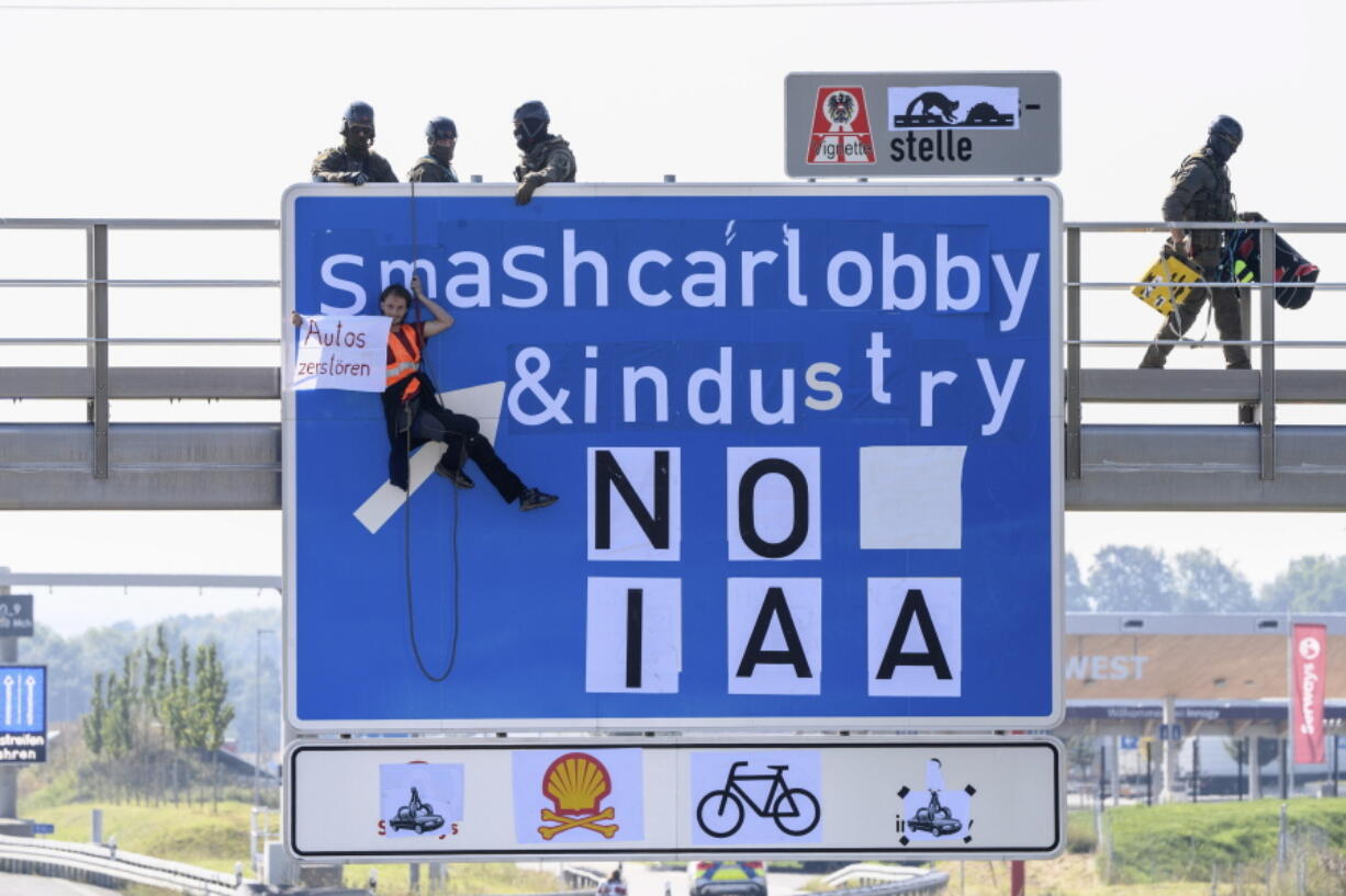 An activist hangs from a gantry over the A9 motorway near F?rholzen in the direction of Munich during a banner campaign, holding a banner with the words "Destroy cars" in his hands while police officers from a special task force get into position on the gantry, Tuesday, Sept.7, 2021. The activists have pasted over the traffic sign with the words "smashcarlobby & industry - NO IAA".