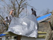 Gary Johnston, left, Grant Boughamer, center, and Jose Garcia, right, place a tarp on a roof damaged by Hurricane Ida, Thursday, Sept. 2, 2021, in Golden Meadow, La. (AP Photo/David J.