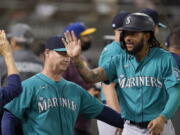 Seattle Mariners' J.P. Crawford, right, is congratulated by manager Scott Servais, left, and teammates after scoring a run against the Oakland Athletics during the third inning of a baseball game in Oakland, Calif., Monday, Sept. 20, 2021.