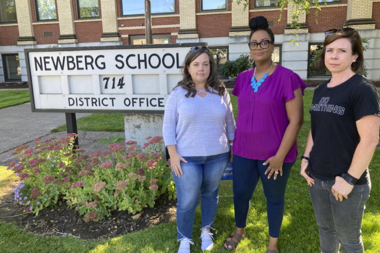 From left, Beth Woolsey, Tai Haden-Moore and AJ Schwanz , who are members of a group called Newberg Equity in Education which is advocating for inclusion and equity in schools, stand in front of a school district office in Newberg, Ore., on Tuesday, Sept. 21, 2021. The Newberg School Board has banned educators from displaying Black Lives Matter and gay pride symbols, prompting a torrent of recriminations and threats to boycott the town and its businesses.