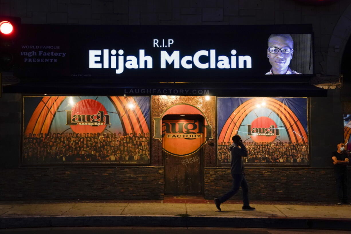 FILE - In this Aug. 24, 2020, file photo, a man walks past a display showing an image of Elijah McClain outside Laugh Factory during a candlelight vigil for McClain in Los Angeles.   Colorado's attorney general said Wednesday, Sept. 1, 2021 that a grand jury indicted three officers and two paramedics in the death of Elijah McClain, a Black man who was put in a chokehold and injected with a powerful sedative two years ago in suburban Denver. (AP Photo/Jae C.