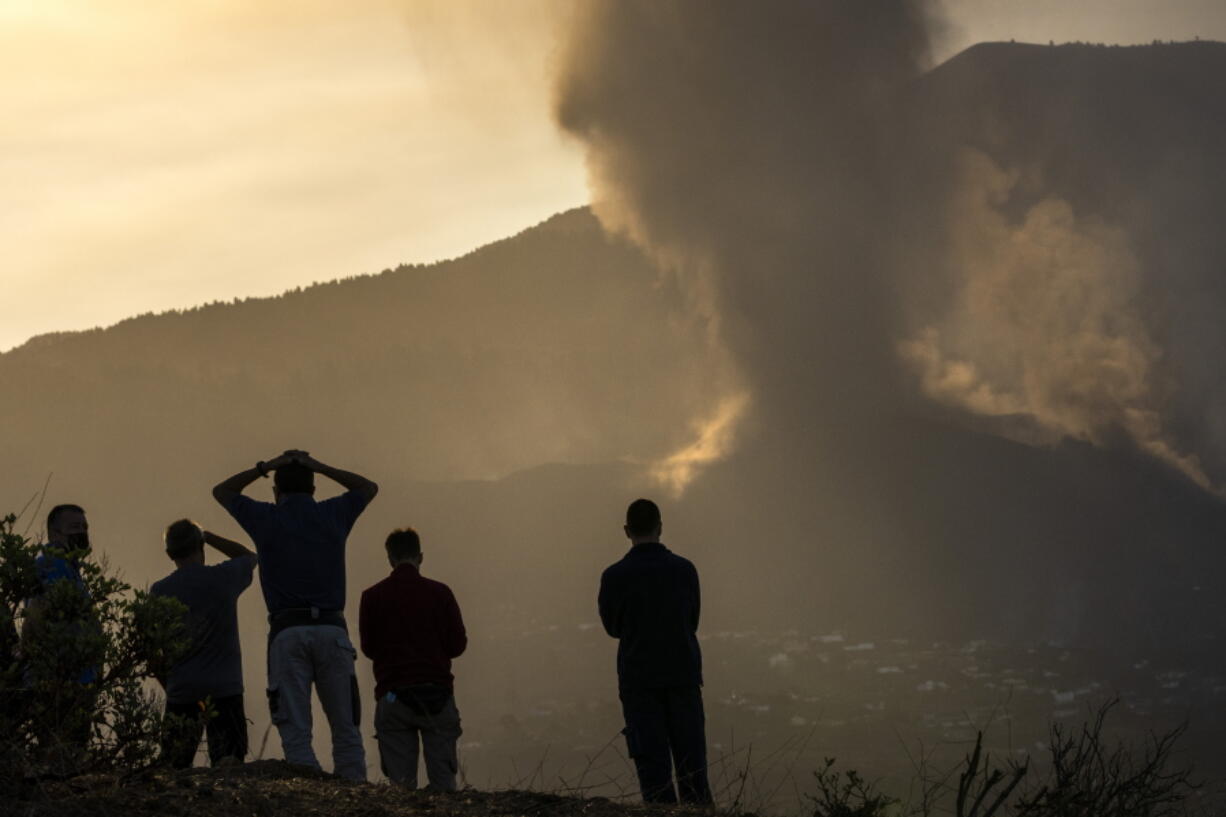 Residents look from a hill as lava continues to flow from an erupted volcano, on the island of La Palma in the Canaries, Spain, Friday, Sept. 24, 2021. A volcano in Spain's Canary Islands continues to produce explosions and spew out lava, five days after it erupted. Two rivers of lava continue to slide slowly down the hillside of La Palma on Friday.