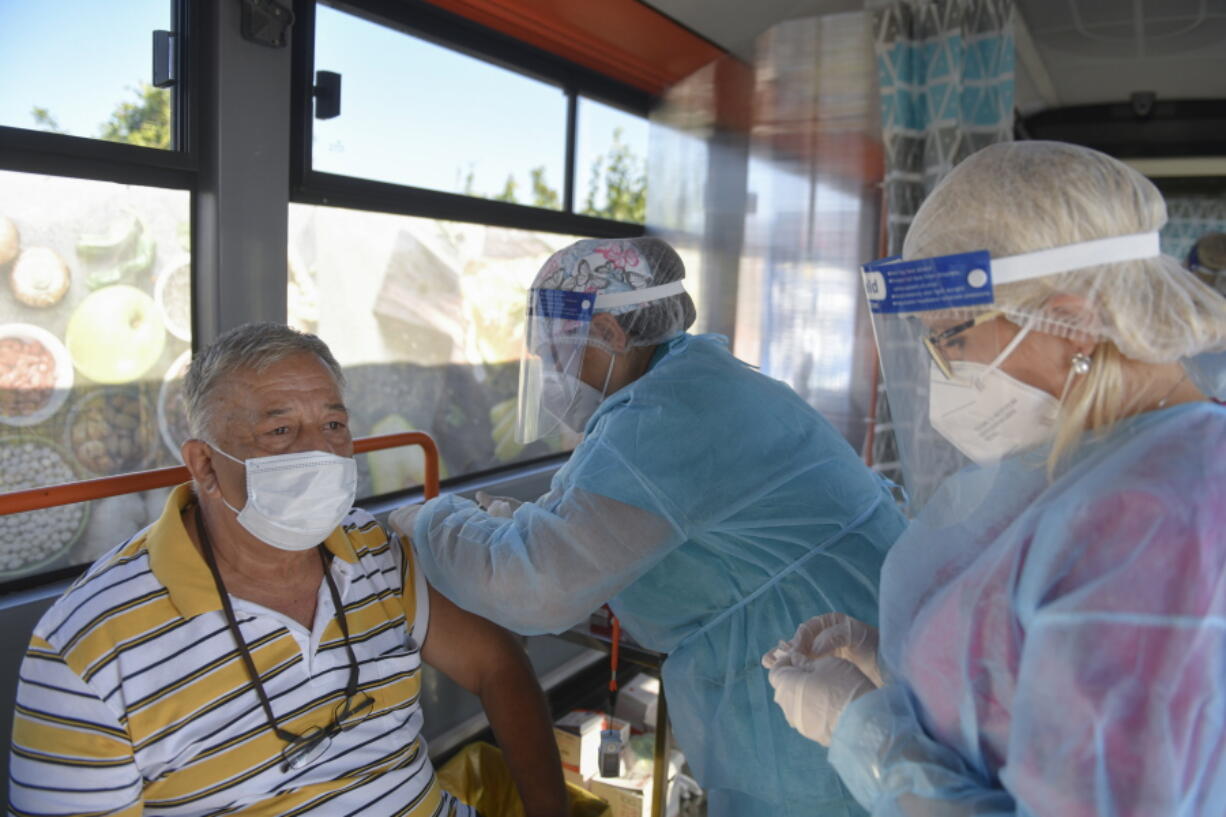 FILE - In this Sept. 4, 2021, file photo, a man receives the Johnson & Johnson vaccine in a bus that serves as a mobile COVID-19 vaccination unit in Bucharest, Romania. In both the U.S. and the EU, officials are struggling with the same question: how to boost vaccination rates to the max and end a pandemic that has repeatedly thwarted efforts to control it. In the European Union, officials in many places are requiring people to show proof of vaccination, a negative test or recent recovery from COVID-19 to participate in everyday activities -- even sometimes to go to work.